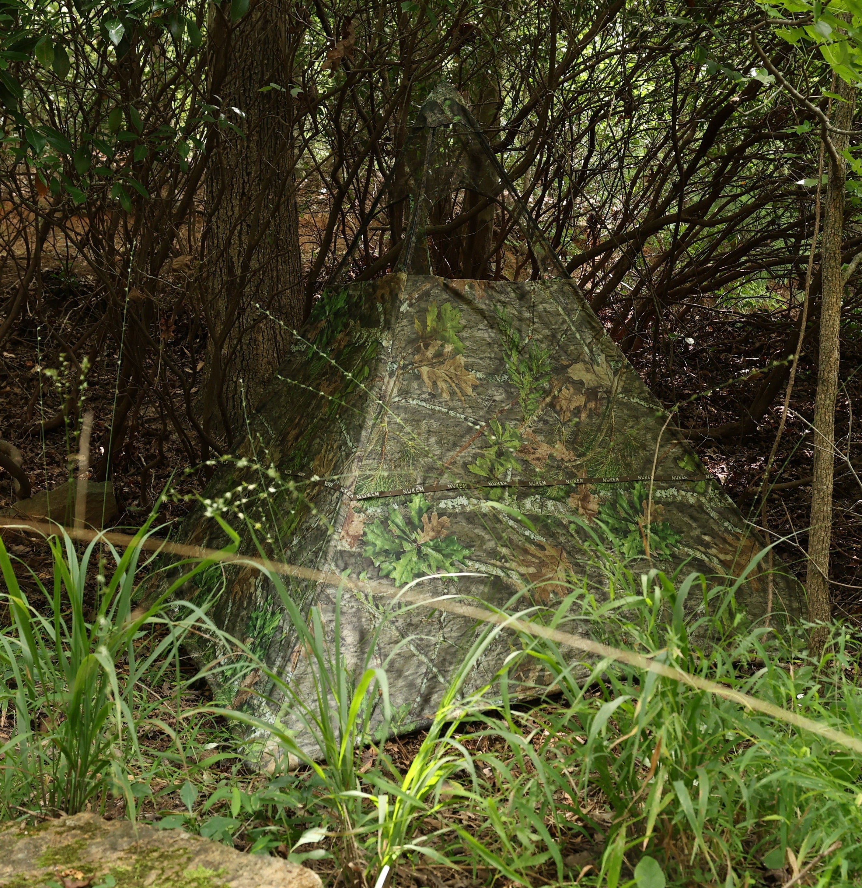 Camo hunting blind with leaf and bark pattern, blending into forest underbrush for stealthy wildlife observation.