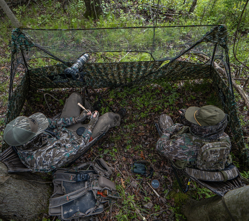 Hunters in camo gear using ground blind with camera setup in forest