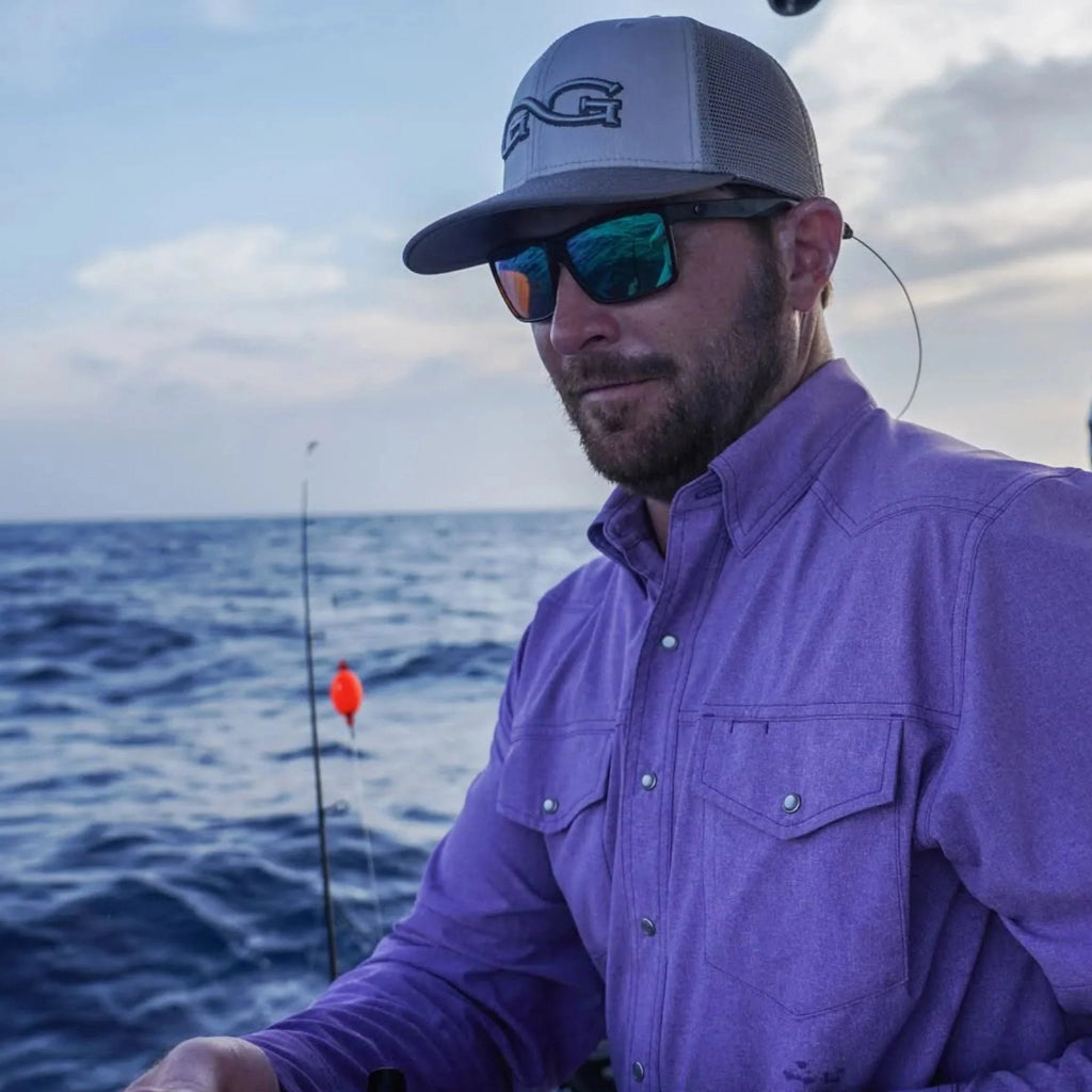 Man fishing on boat wearing purple long sleeve shirt, gray trucker hat, and polarized sunglasses