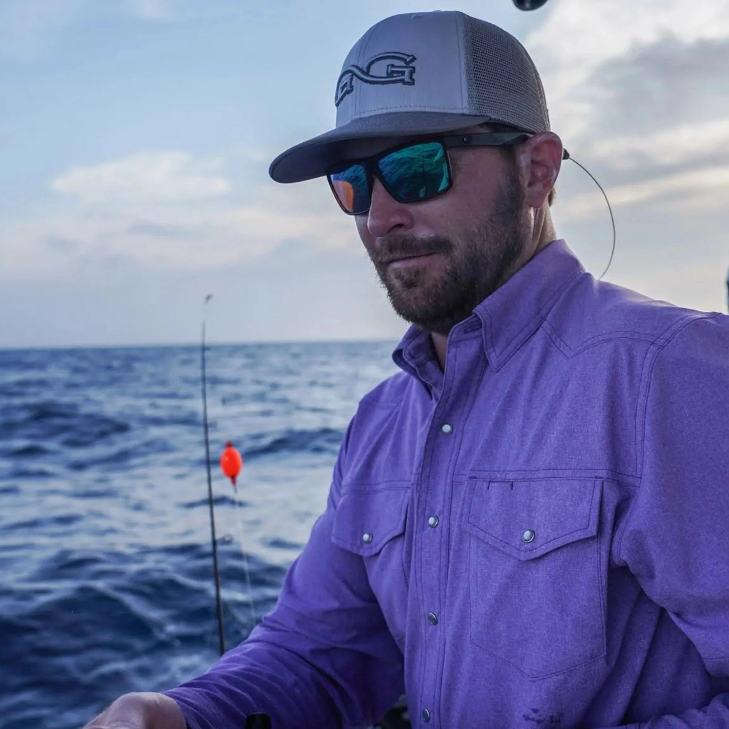 Man fishing on boat wearing purple long sleeve shirt, gray trucker hat, and polarized sunglasses