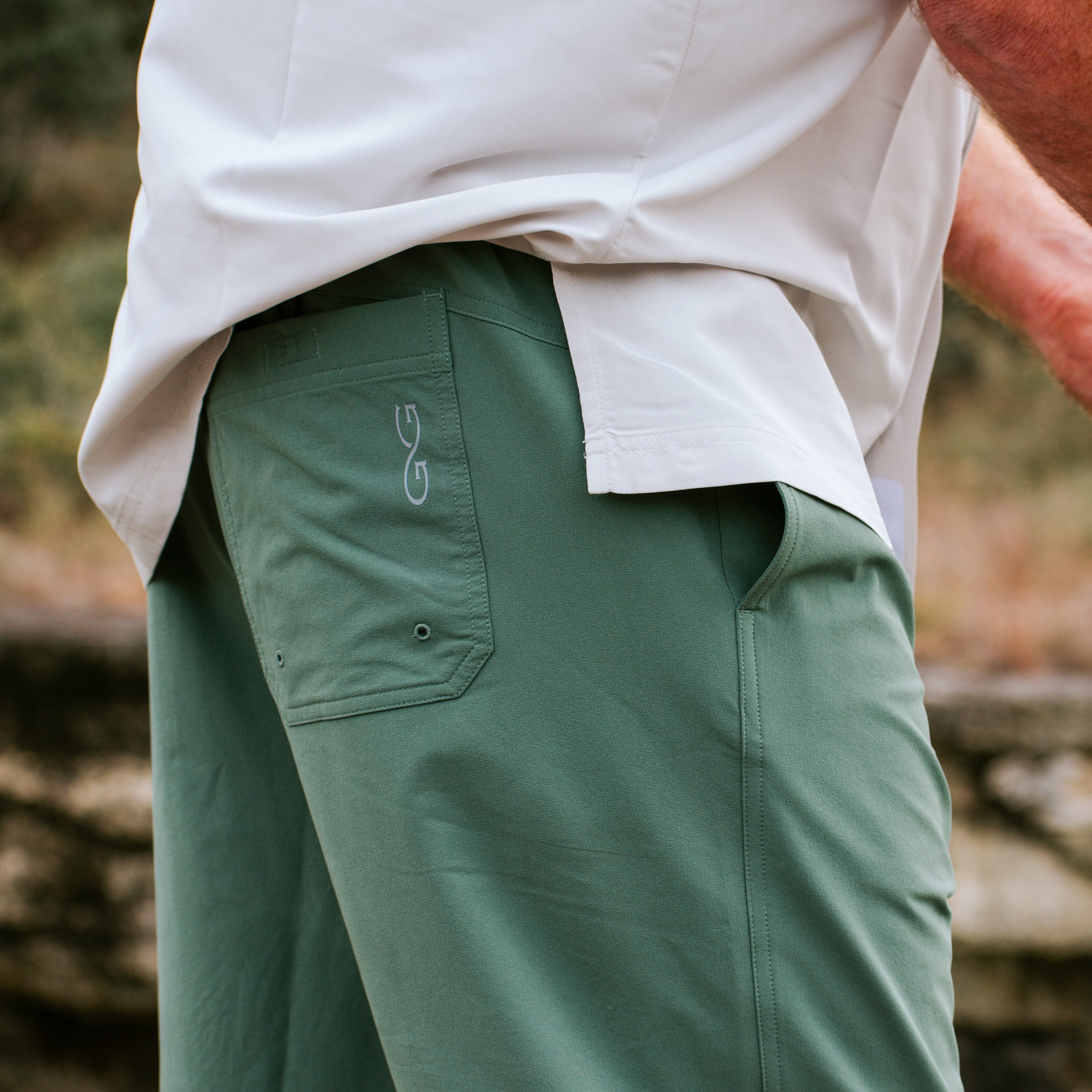 Green hunting pants with logo, worn with white shirt for outdoor adventures