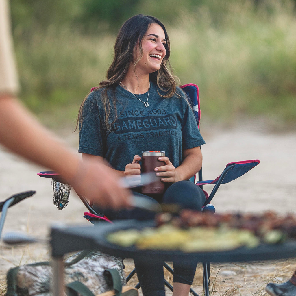 Woman in GameGuard tee enjoying outdoor camping with insulated tumbler, perfect for hunting and fishing adventures.