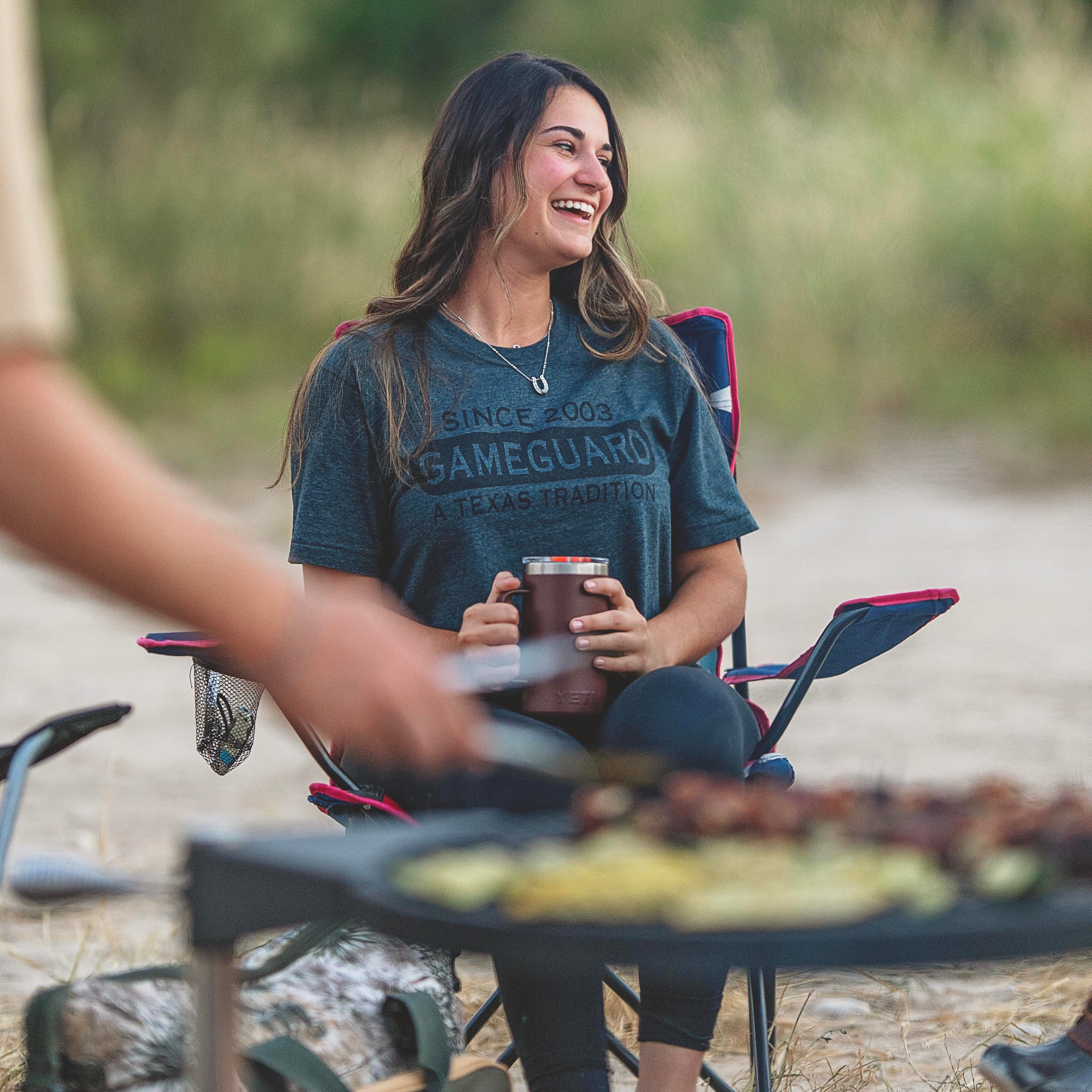 Woman in GameGuard tee enjoying outdoor camping with insulated tumbler, perfect for hunting and fishing adventures.