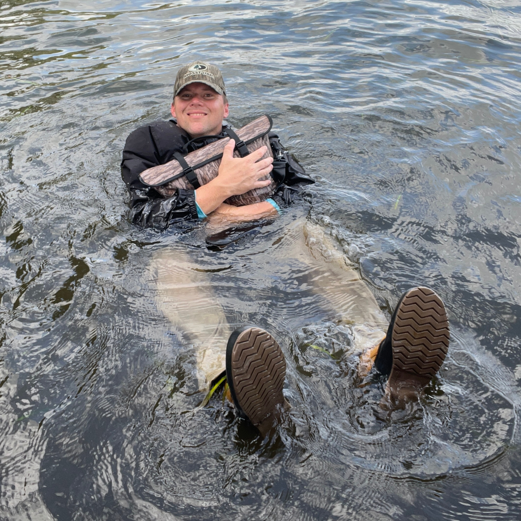 Man floating in water wearing waterproof waders and camo hat, holding camo float tube for fishing or hunting