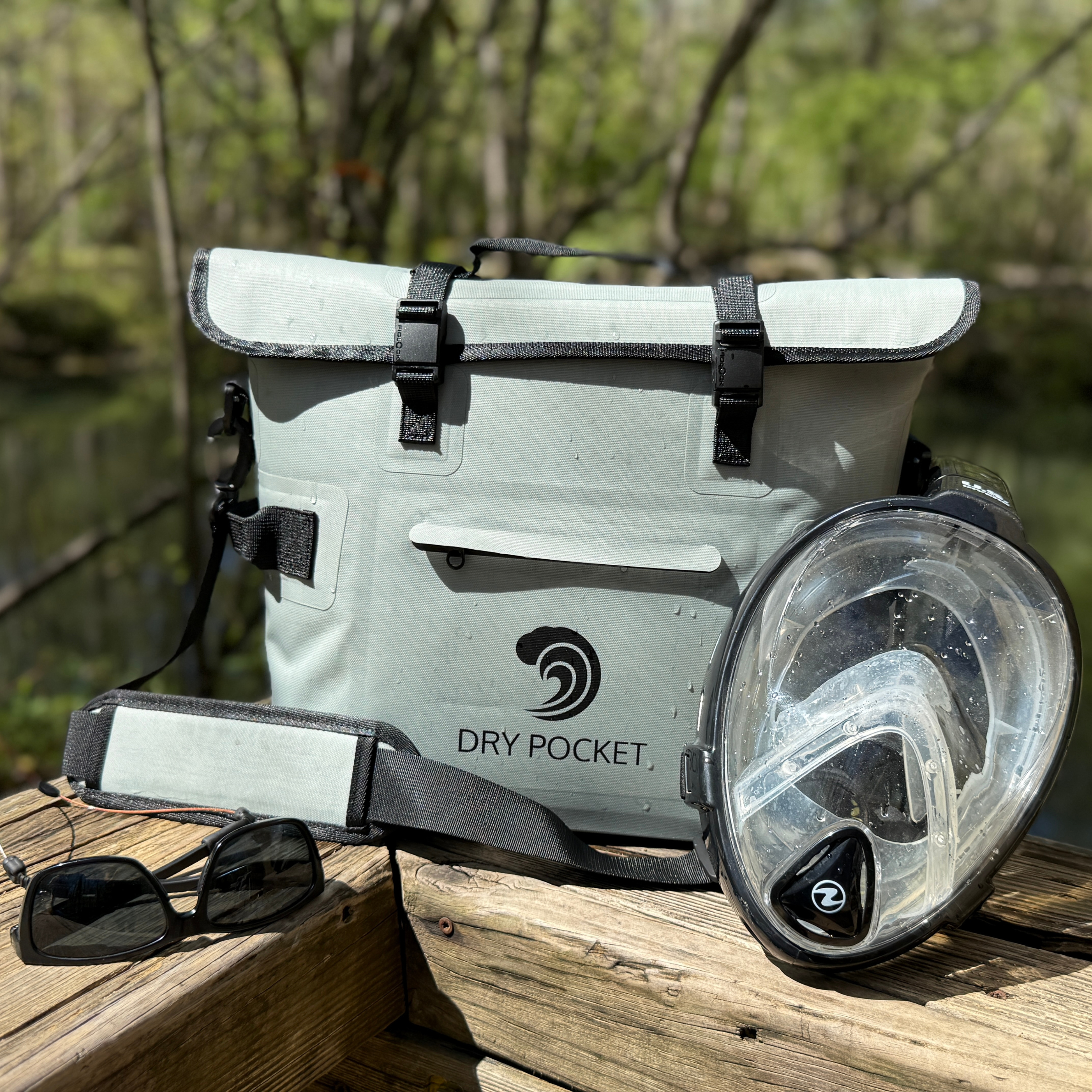 Light gray Dry Pocket waterproof dry bag with full-face snorkel mask and sunglasses on wooden dock, ideal for fishing and outdoor adventures.