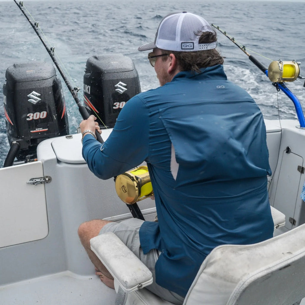 Man fishing offshore in blue long sleeve shirt and white cap, using heavy tackle on boat with Suzuki 300 motors