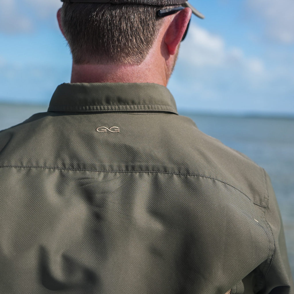 Olive green outdoor shirt with GG logo, worn by man near water, ideal for fishing and hunting adventures.