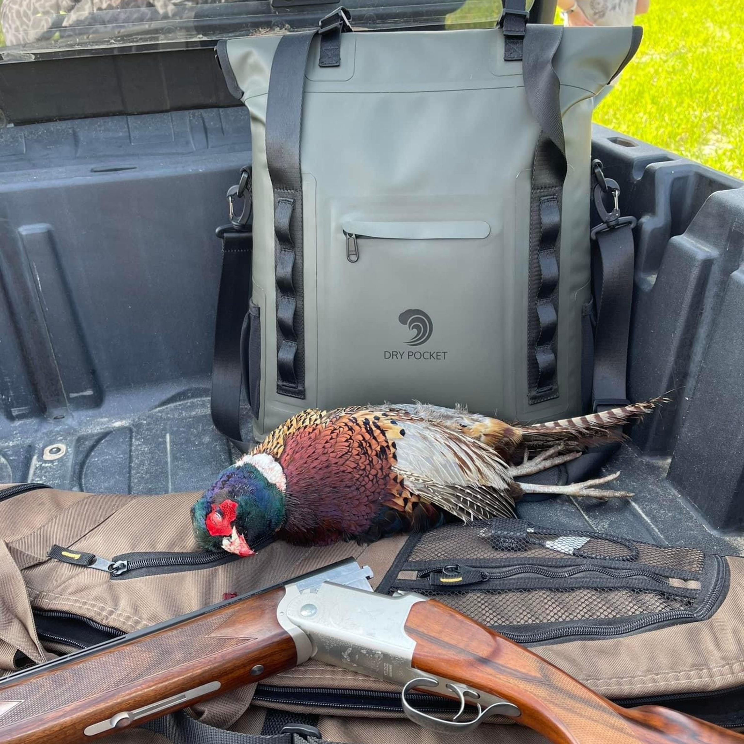 Hunting gear: shotgun, pheasant, and Dry Pocket waterproof backpack in truck bed for outdoor adventures.