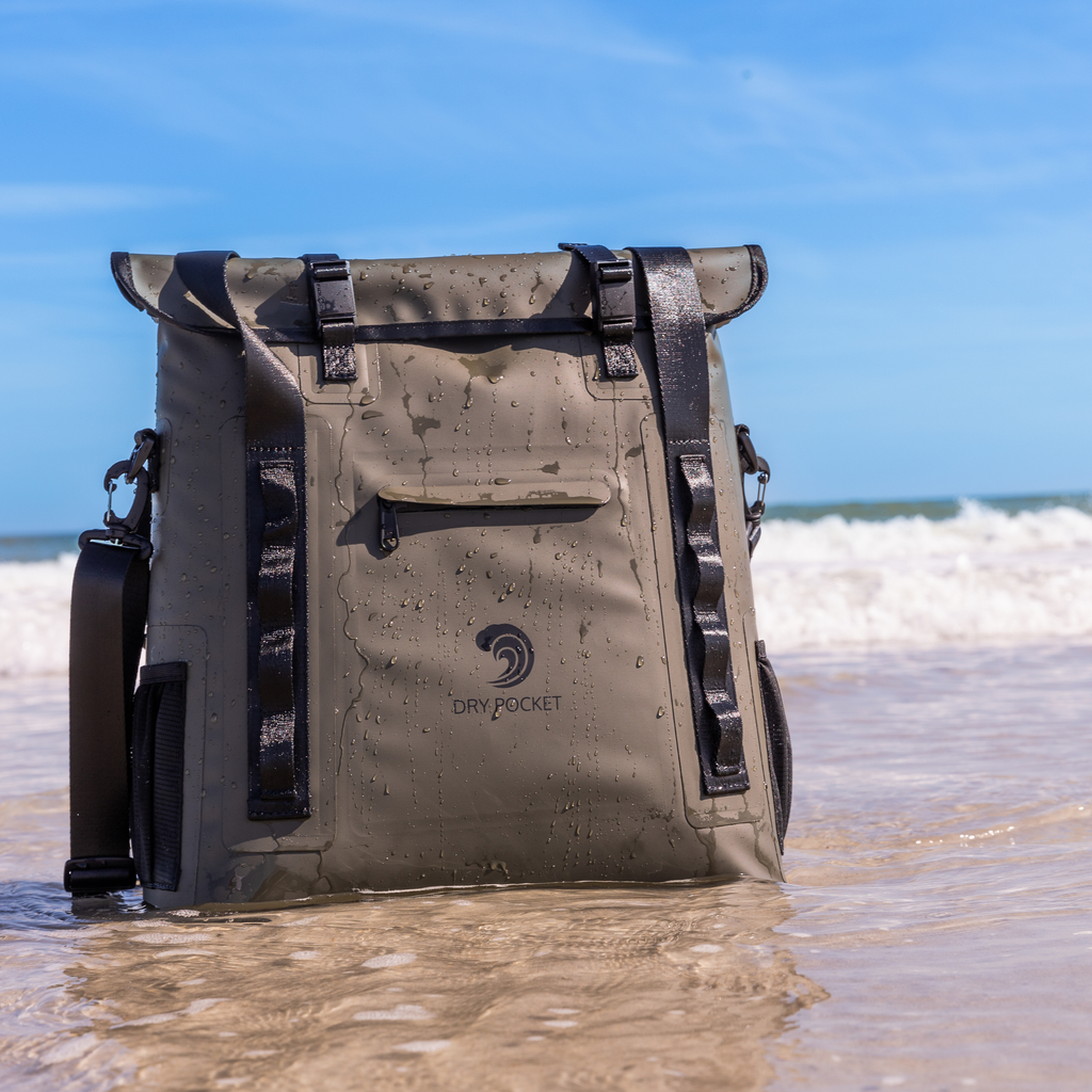Olive dry bag with black straps standing in ocean waves, waterproof gear for hunting and fishing adventures