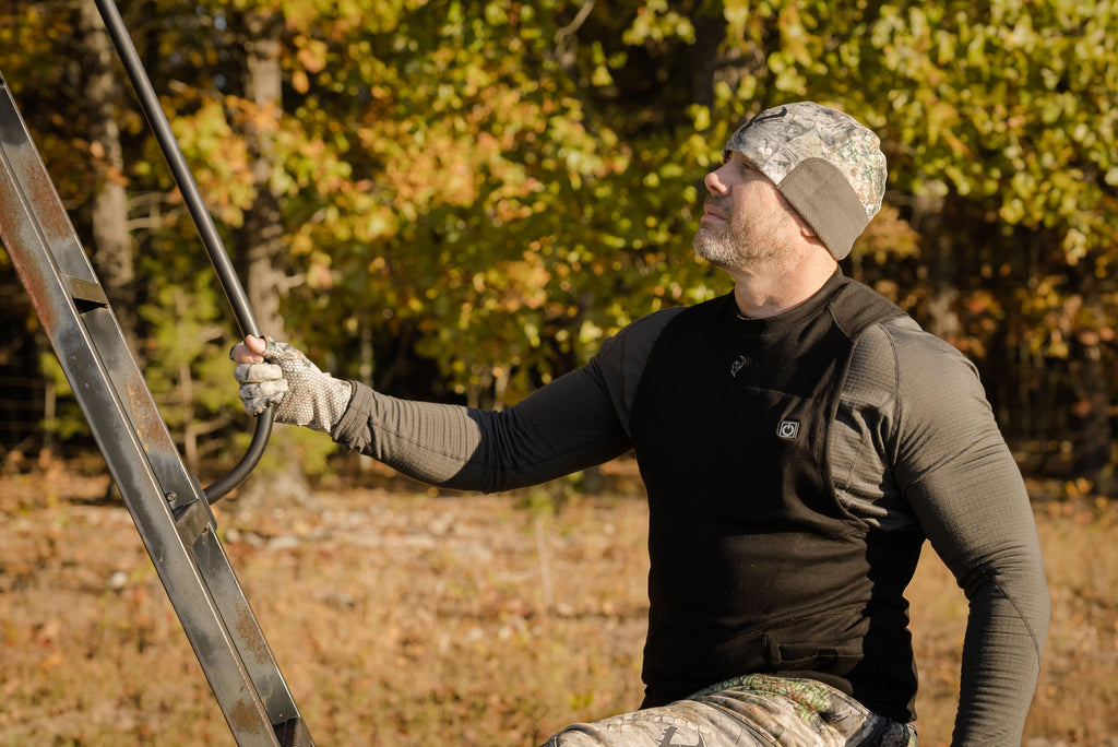 Hunter wearing a Vycah Pyrex Extreme charcoal base layer shirt and camo beanie while setting a ladder stand