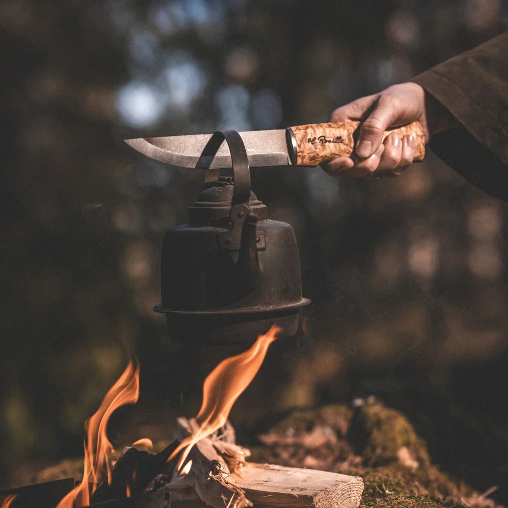 Hunting knife with wooden handle held over campfire, outdoor survival gear