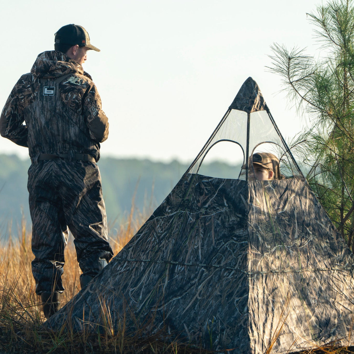 Camo hunting blind with mesh windows for concealment in field, used with matching camo gear for deer hunting