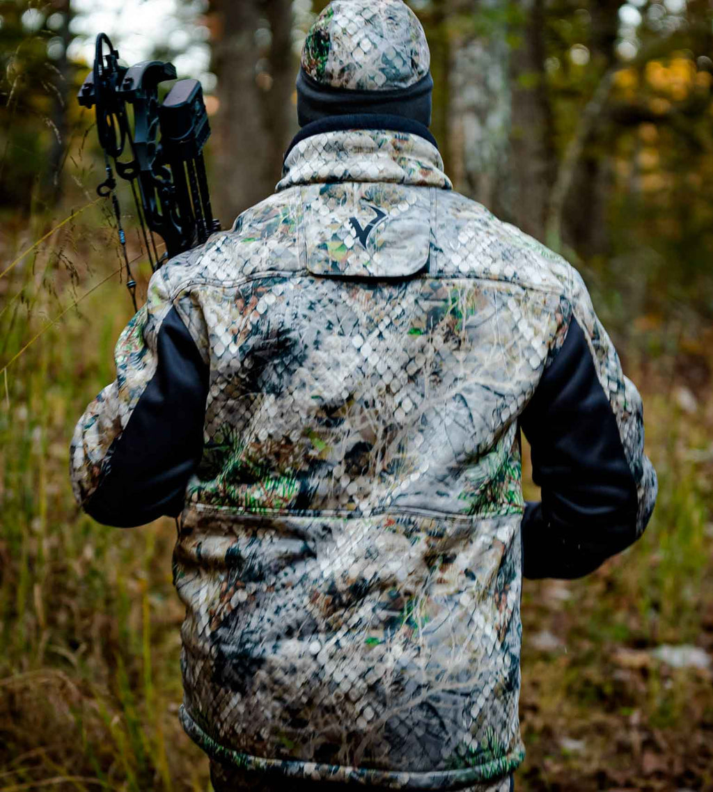 Hunter seen from behind wearing a Vycah Kinsley Jacket and camo beanie, carrying a compound bow