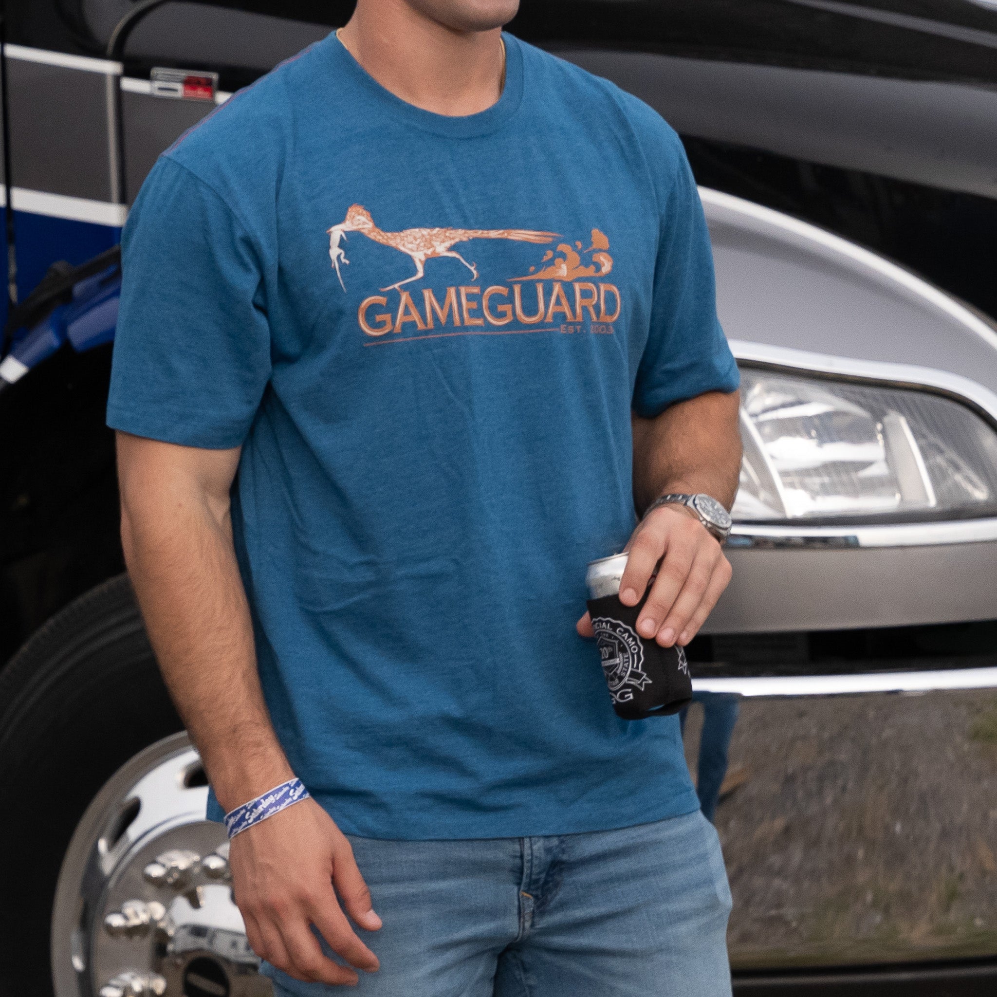 Blue GameGuard hunting t-shirt with roadrunner graphic, worn outdoors near truck