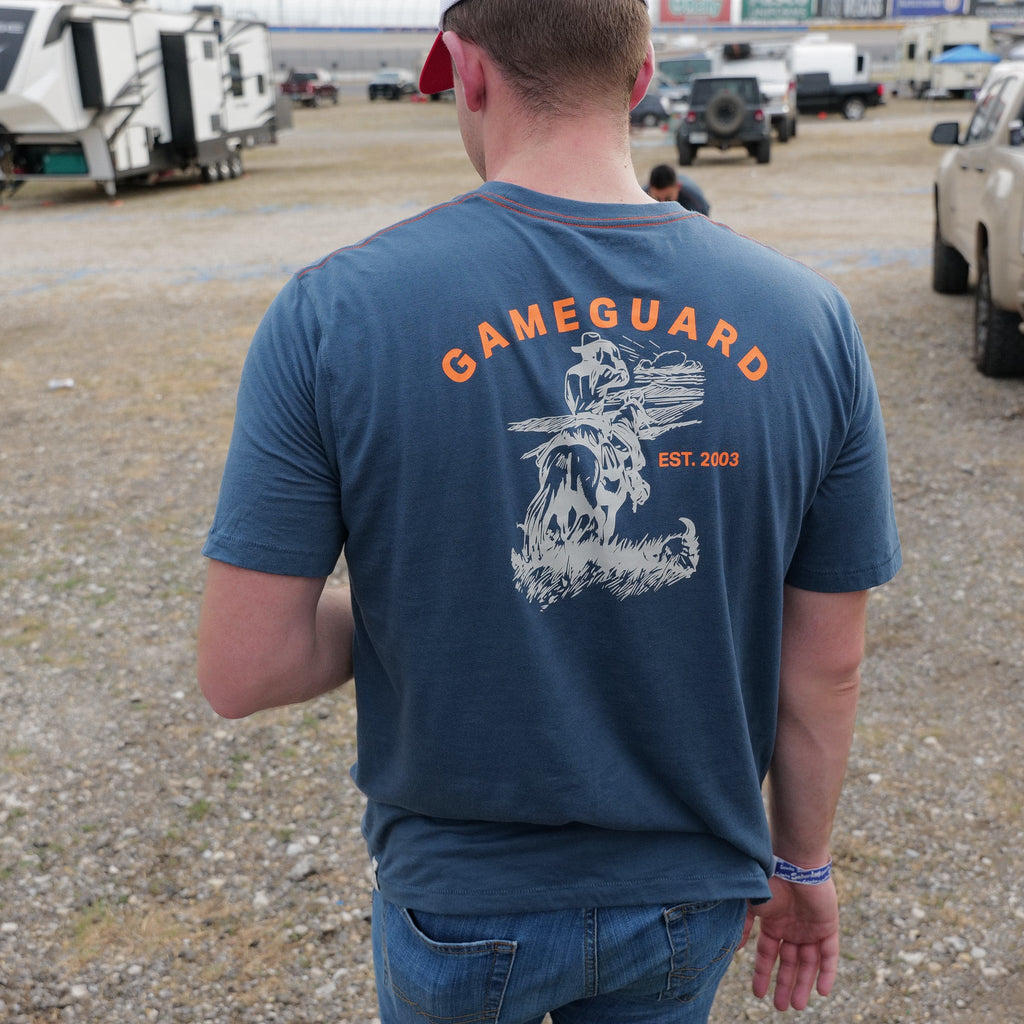 Blue Gameguard hunting t-shirt with orange text and wildlife graphic, worn outdoors at campsite
