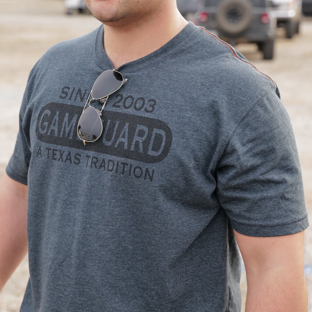 Gray Game Guard t-shirt with 'Since 2003 A Texas Tradition' print, worn outdoors with sunglasses on collar