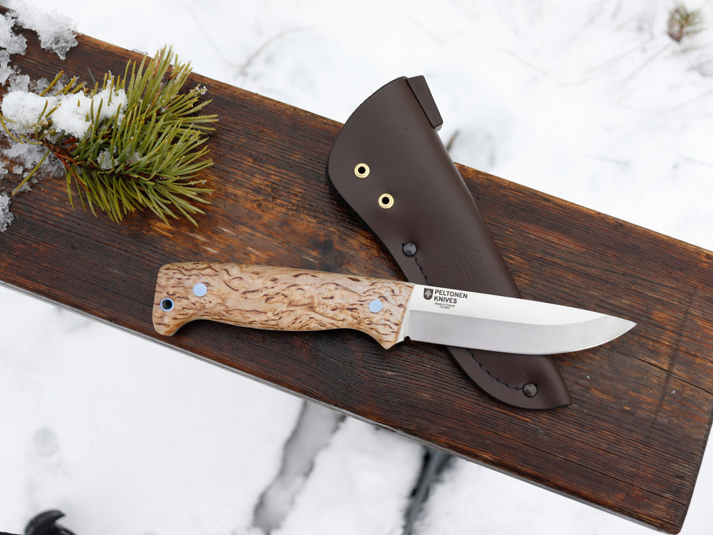 Peltonen hunting knife with burl wood handle and leather sheath on snowy wood, ideal for outdoor survival gear