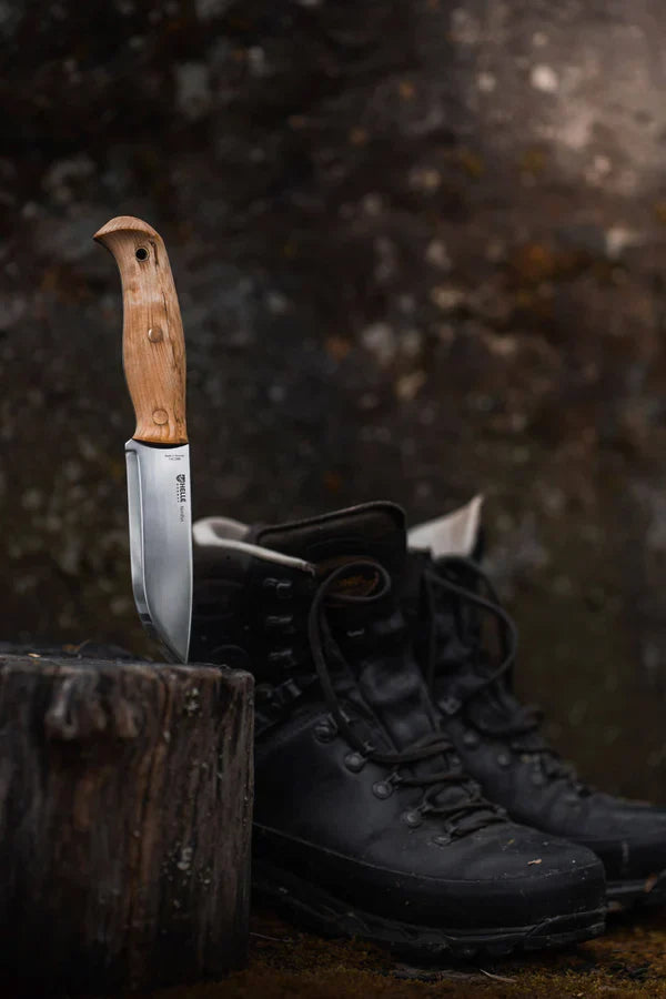 Hunting knife with wooden handle and steel blade beside rugged black boots on forest stump