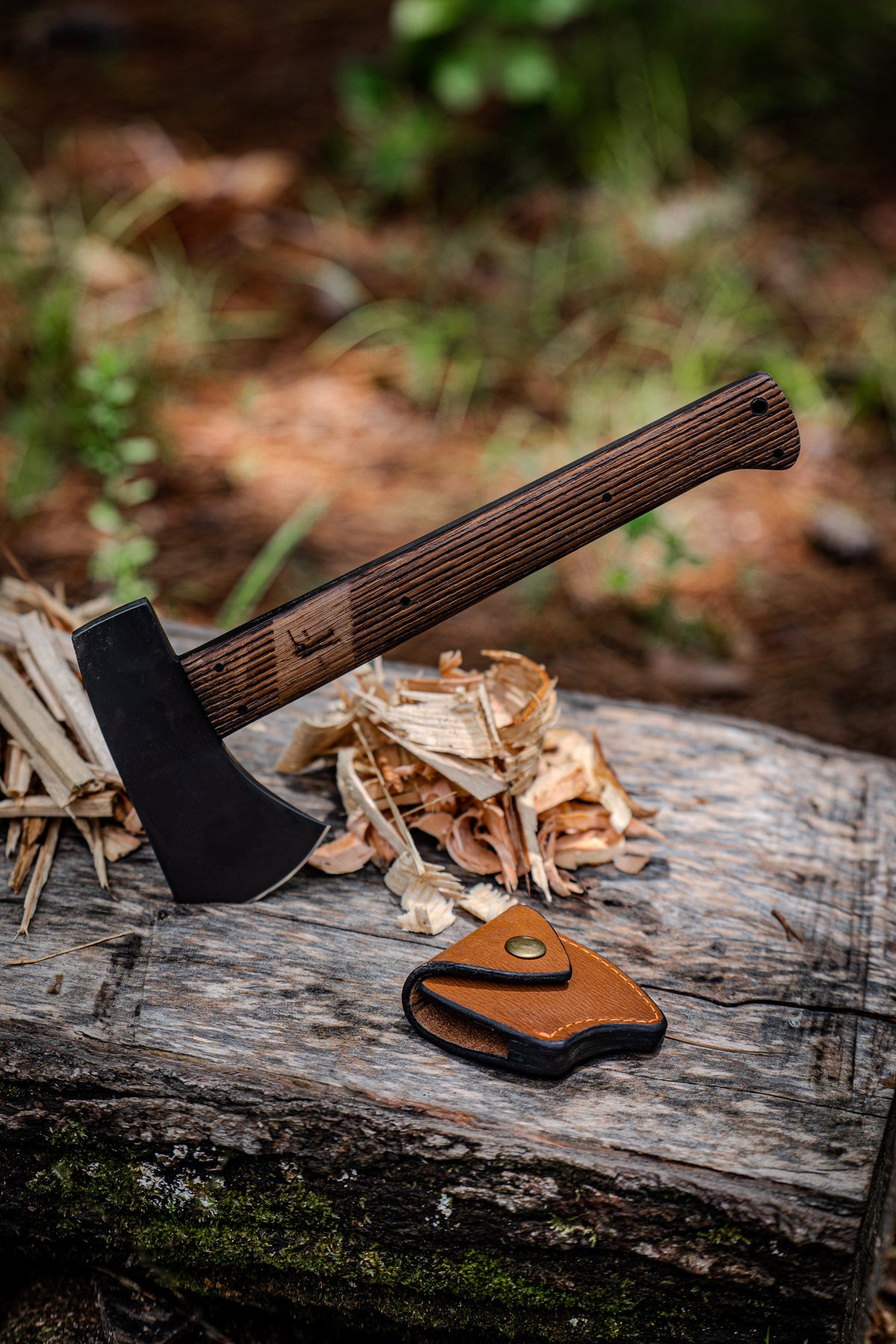 Winkler Highland Hatchet resting on a log with kindling and its leather blade cover