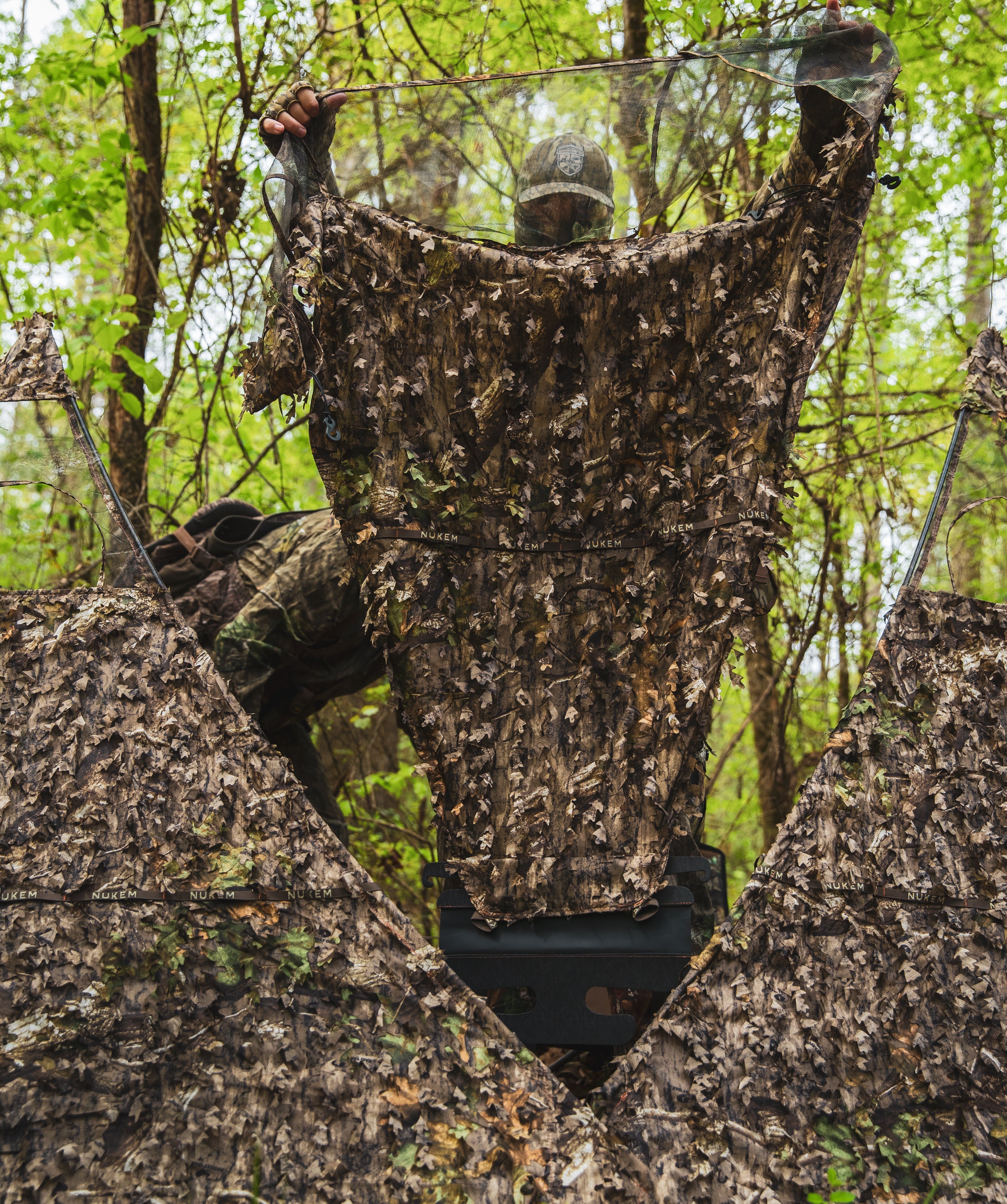 Camouflage hunting blind with leafy pattern for tree stand concealment in forest setting