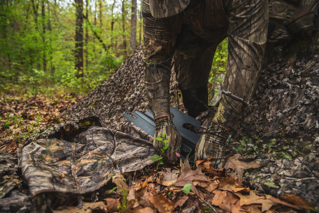 Camo hunting gear in forest, Mossy Oak pattern, outdoor hunting apparel setup