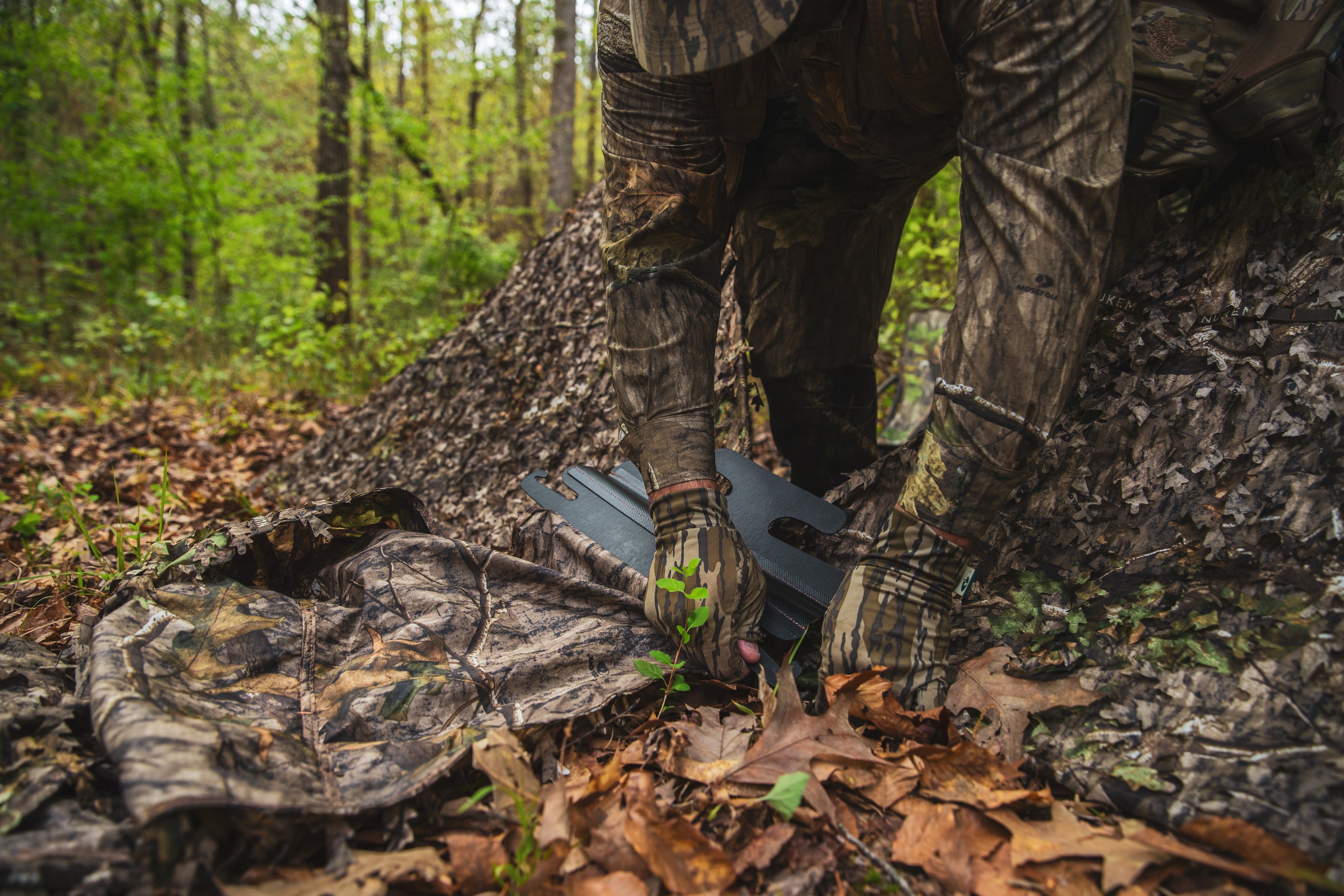 Camo hunting gear in forest, Mossy Oak pattern, outdoor hunting apparel setup