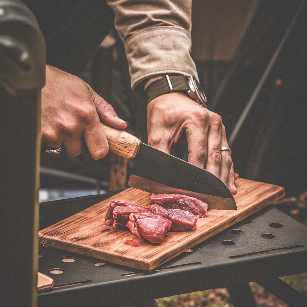 Hunting knife with wooden handle slicing venison on camp cutting board