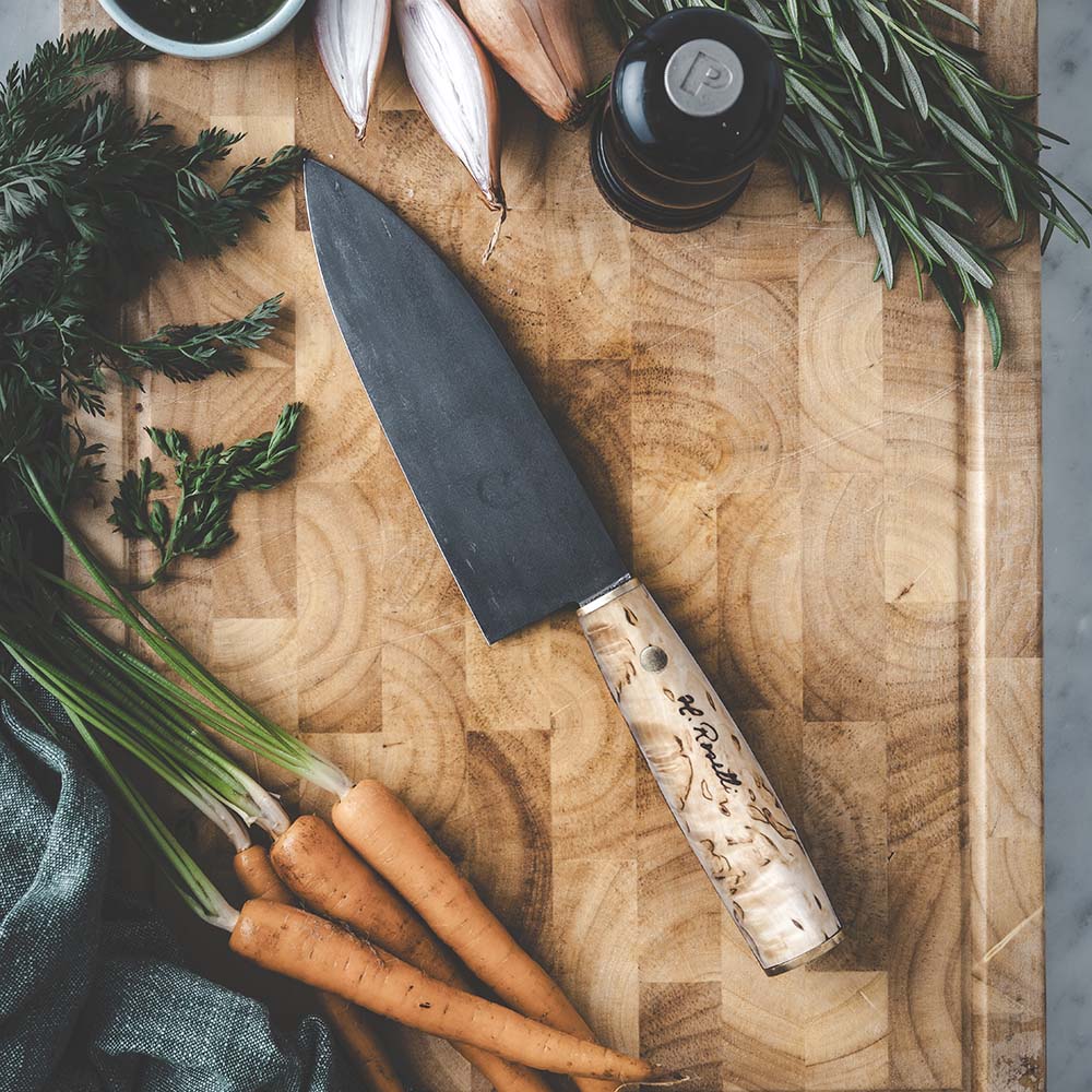 Handcrafted chef knife with birch wood handle on cutting board with fresh herbs and carrots