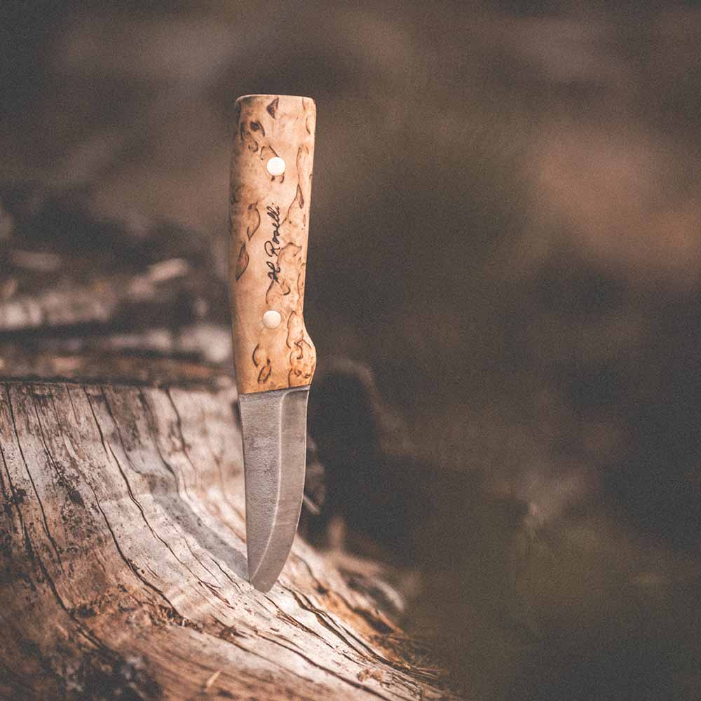 Handmade hunting knife with burl wood handle, stainless steel blade, embedded in tree stump for outdoor use