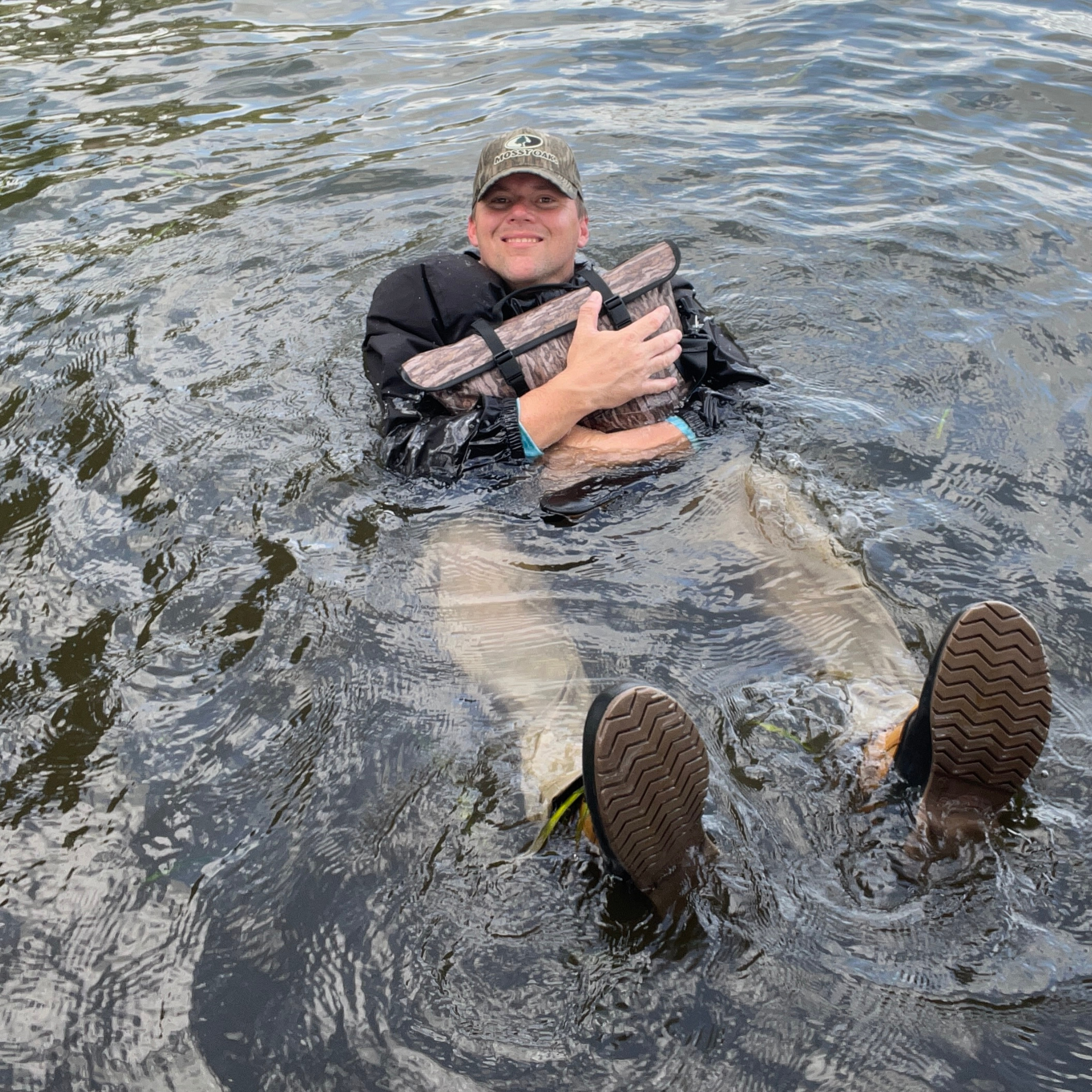 Man floating in water wearing waterproof hunting waders with camo pattern and wading boots