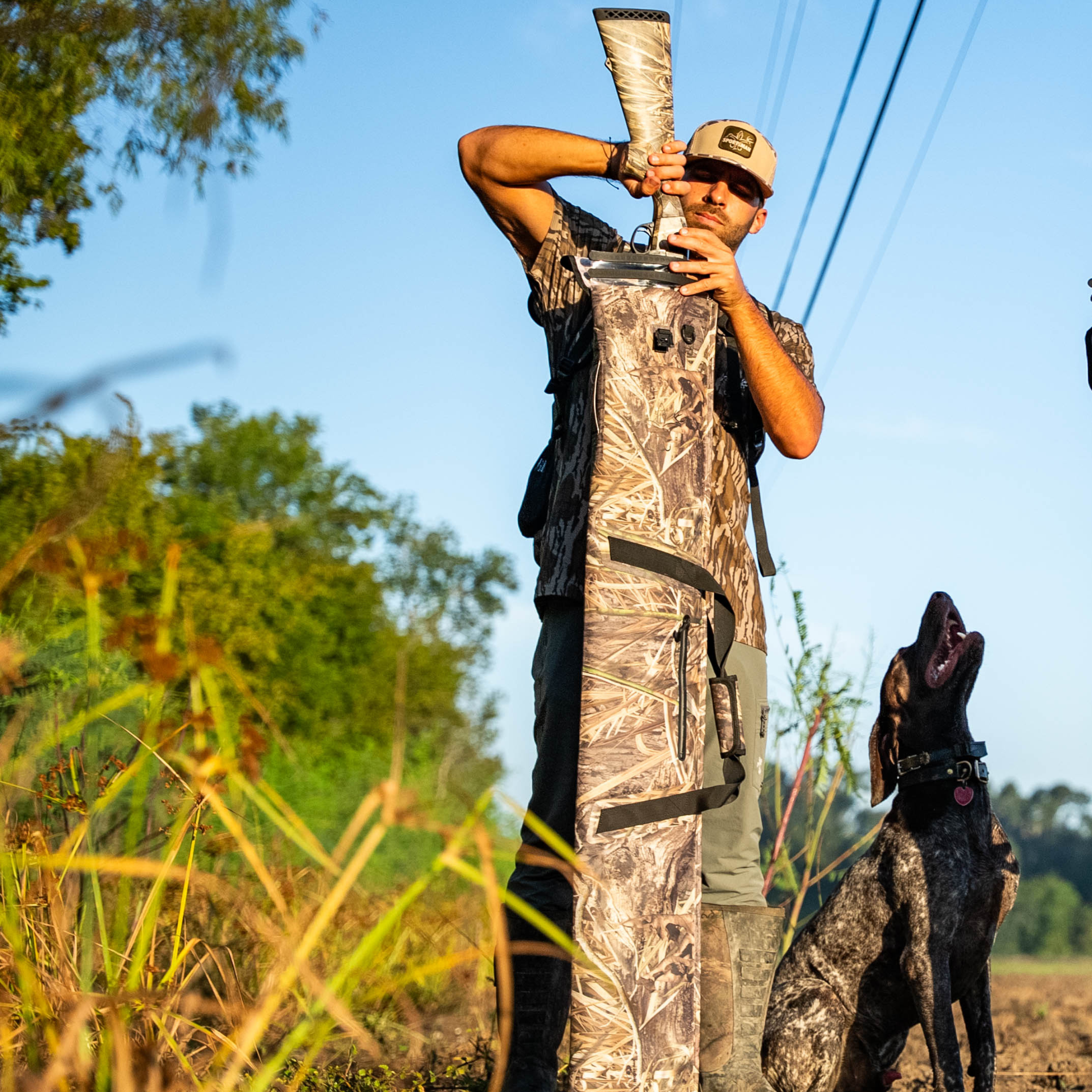 Hunter in camo holding shotgun with dog, outdoor hunting gear for wetlands and field use