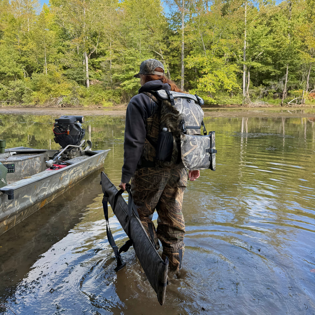 Hunter in camo waders carrying decoy bag near boat in marsh, ideal for duck hunting gear