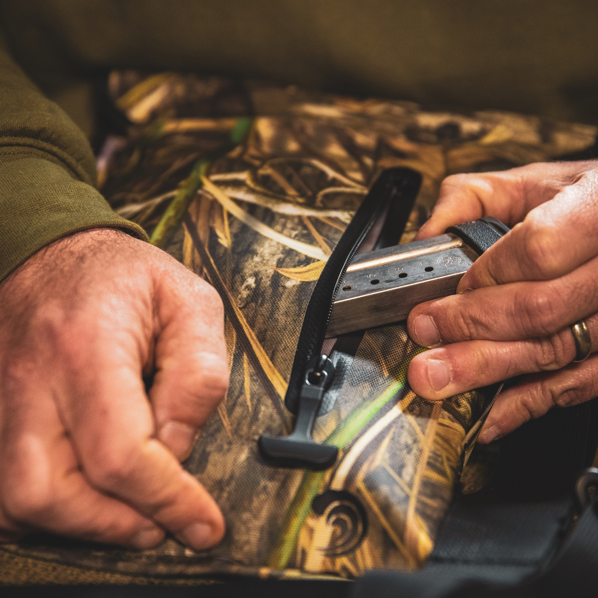 Hunter loading shotgun shells into camo vest pocket, outdoor hunting gear