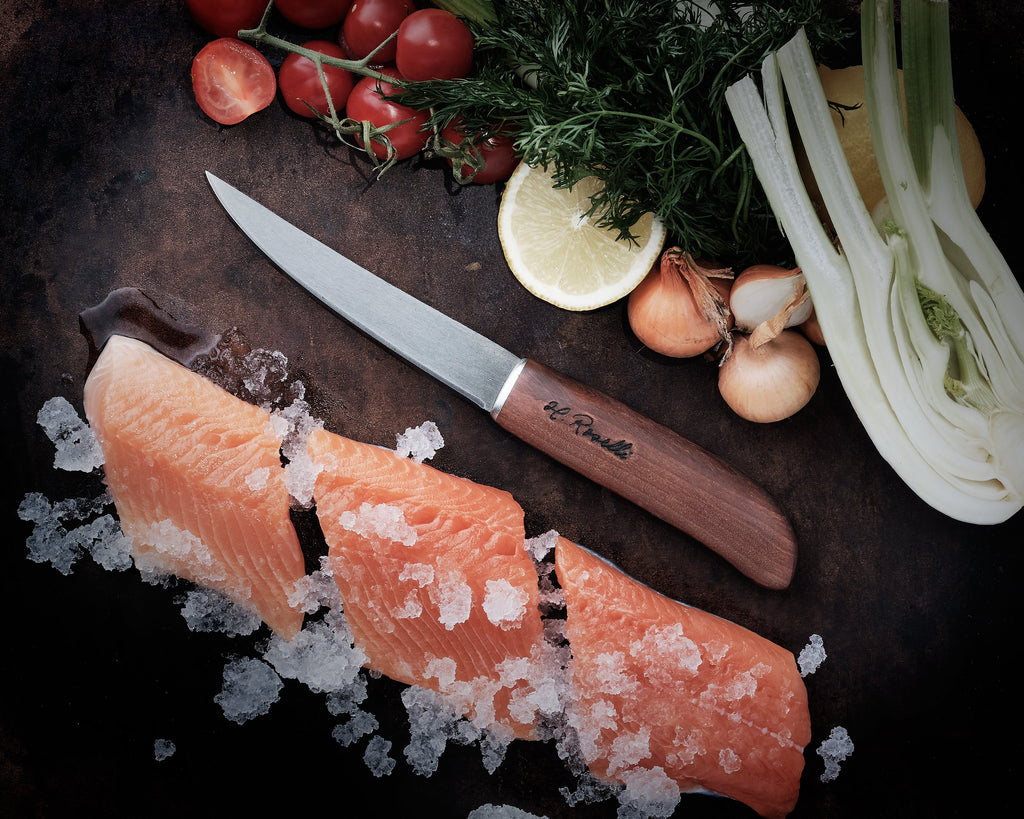 H. Roselli fillet knife with wood handle beside fresh salmon, tomatoes, dill, lemon, and fennel on dark surface