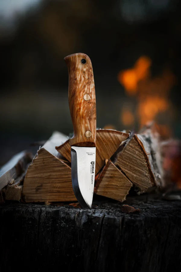 Helle hunting knife with wood handle, stainless steel blade, resting on log near campfire