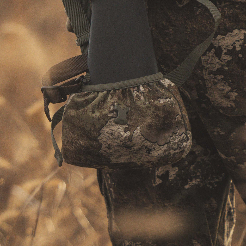 Camo hunting gear pouch with tree bark pattern, attached to rifle stock for outdoor use