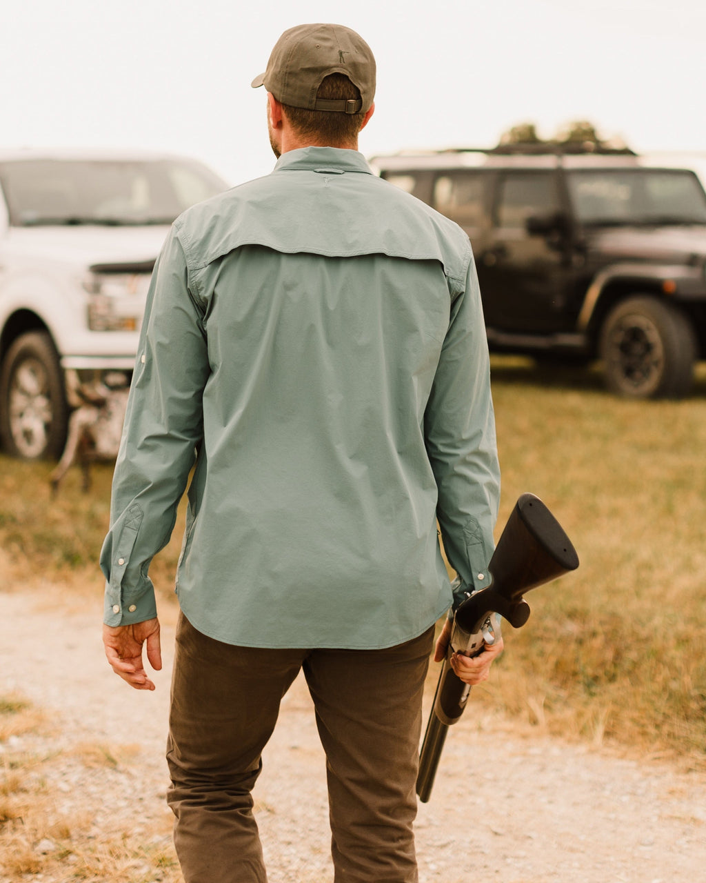 Man carrying a shotgun toward trucks wearing the Heritage Pant
