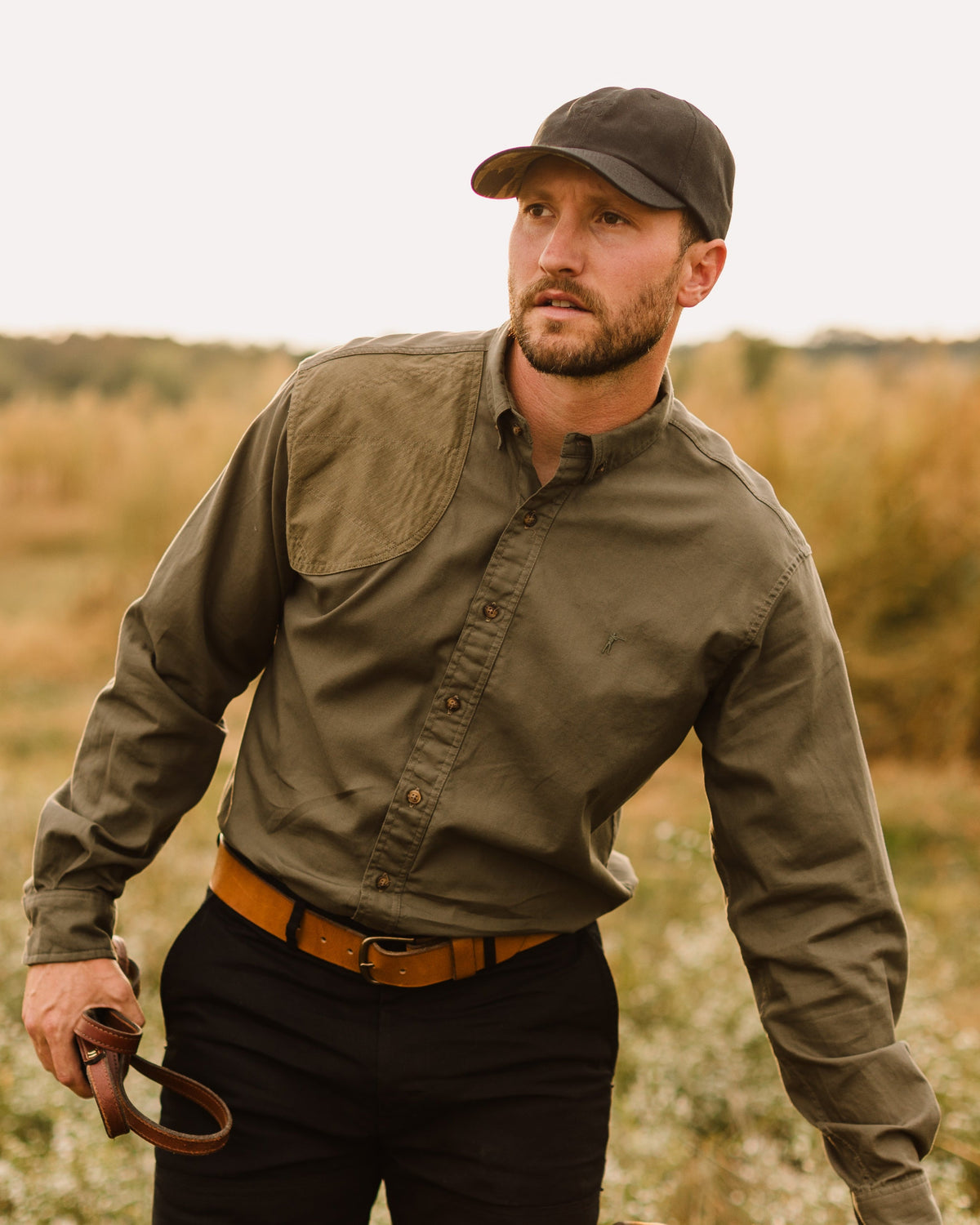 Man in the Jack Carr Hunters Shirt holding a dog lead in a field