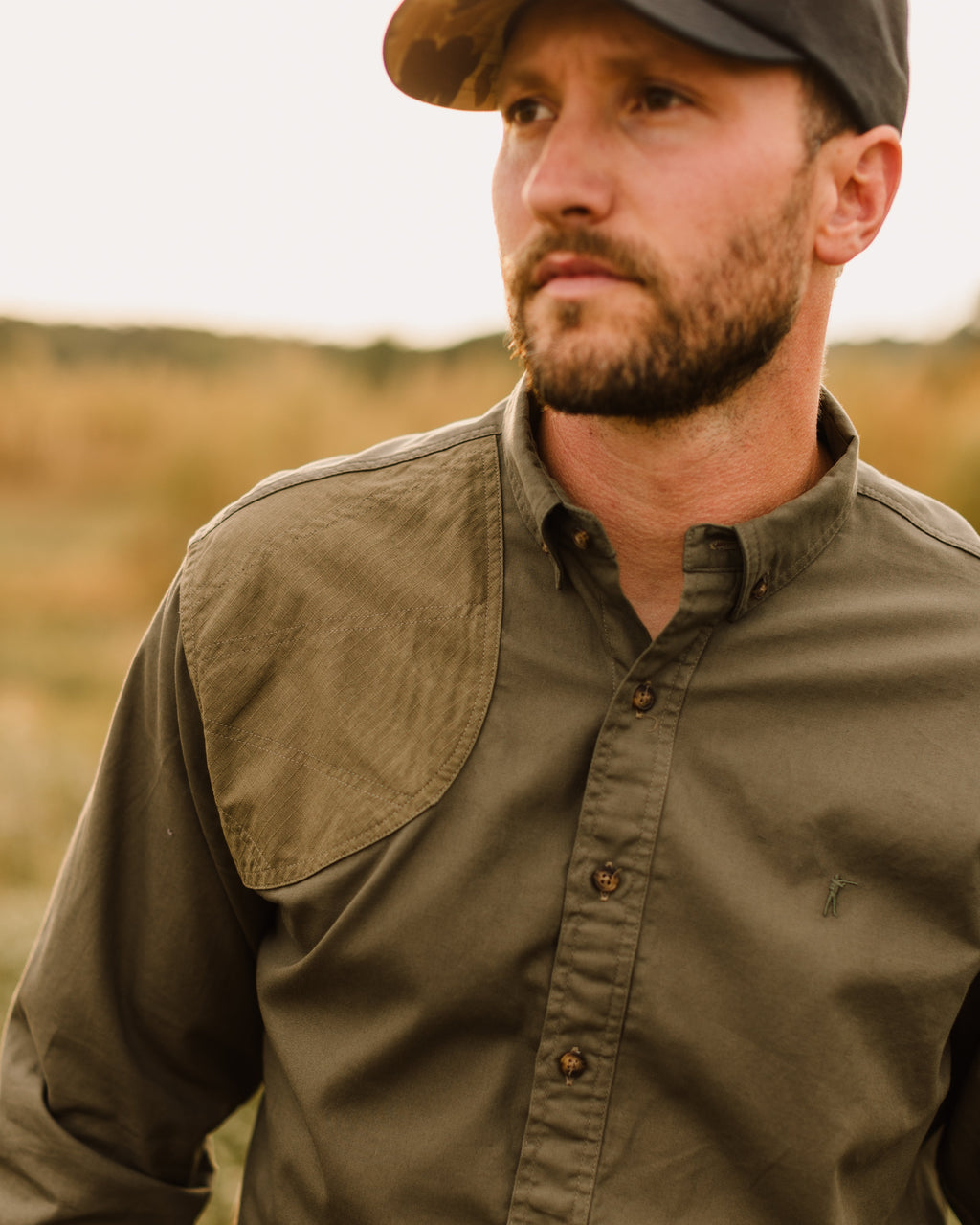 Man in a field cap wearing the Ranger Green Jack Carr Hunters Shirt in a grass field
