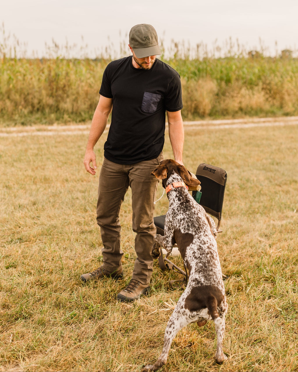 Man in a black tee and Heritage Pant crouching with a bird dog