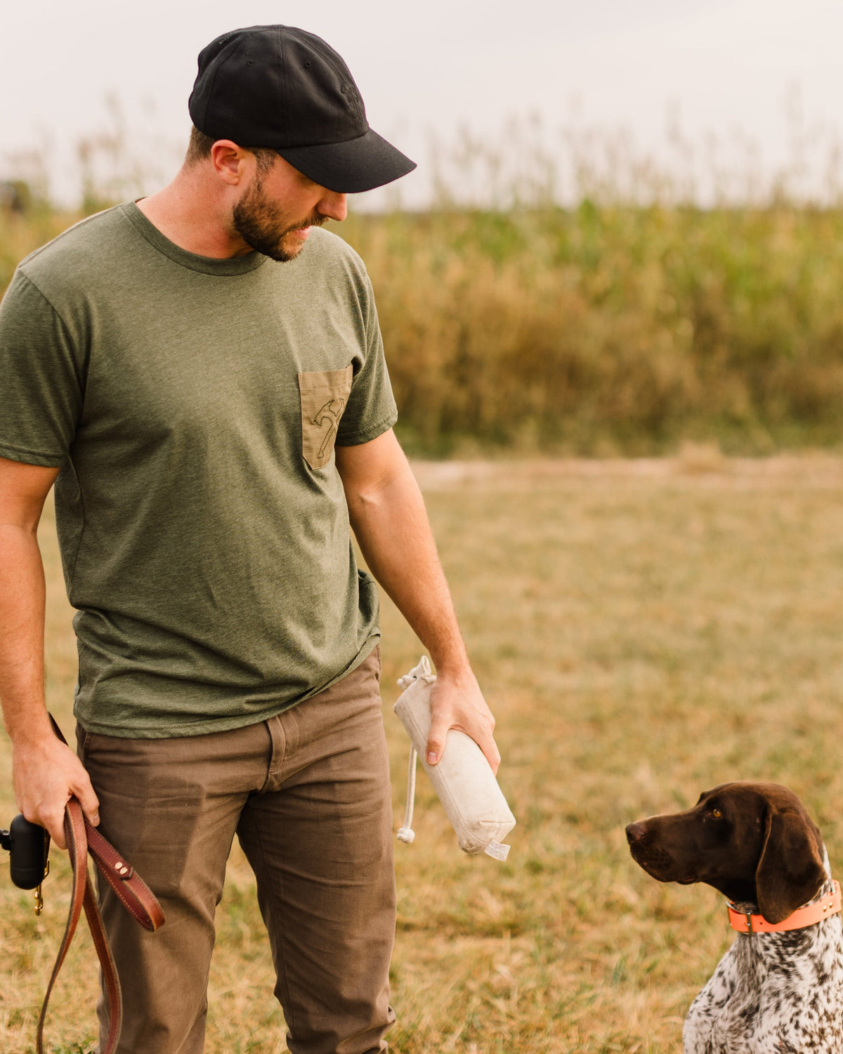 Man in a green tee and Heritage Pant walking with a bird dog