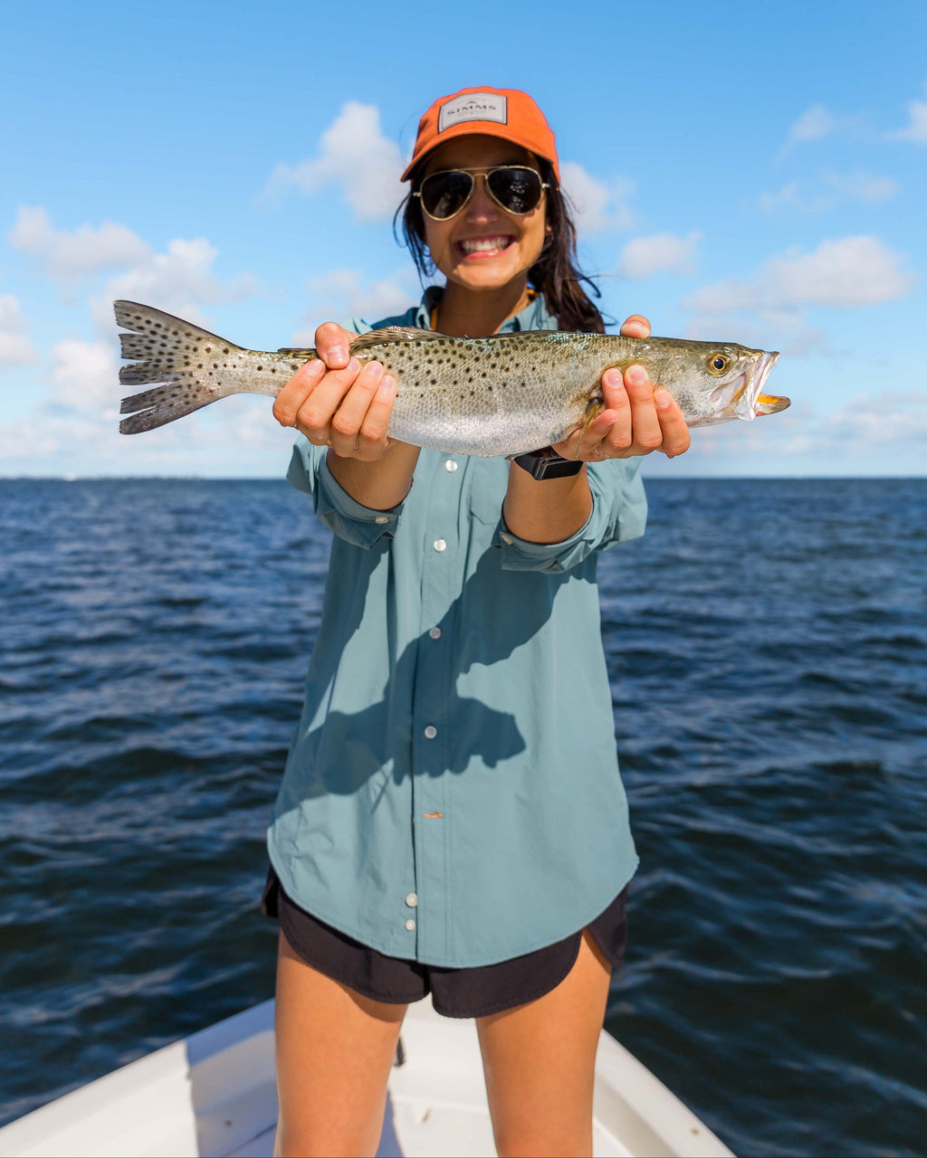 Woman holding a speckled trout on a boat wearing the River Green Active+ Guide Shirt