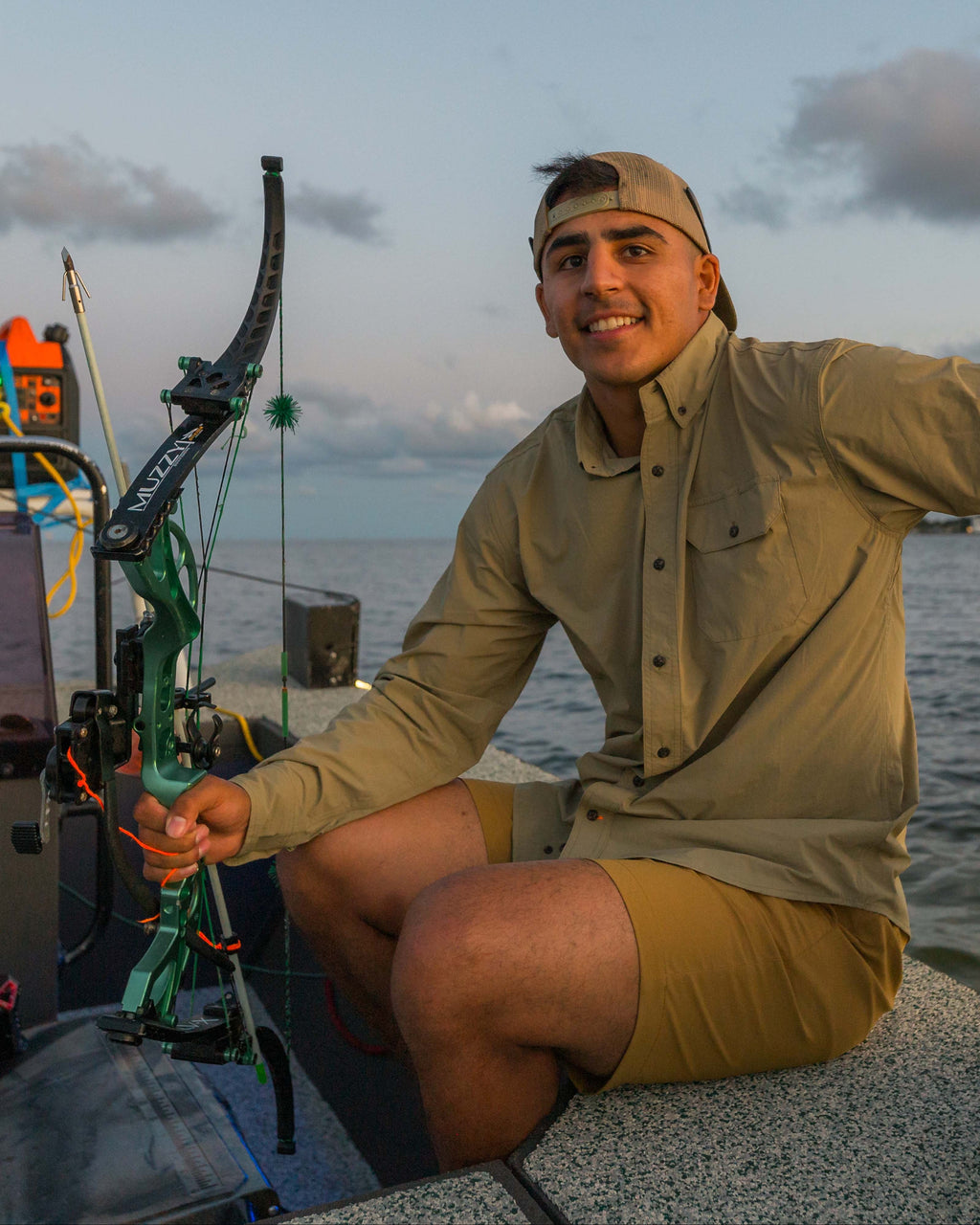 Bowfisherman sitting on a boat deck with a green bow wearing the Tan Active+ Guide Shirt