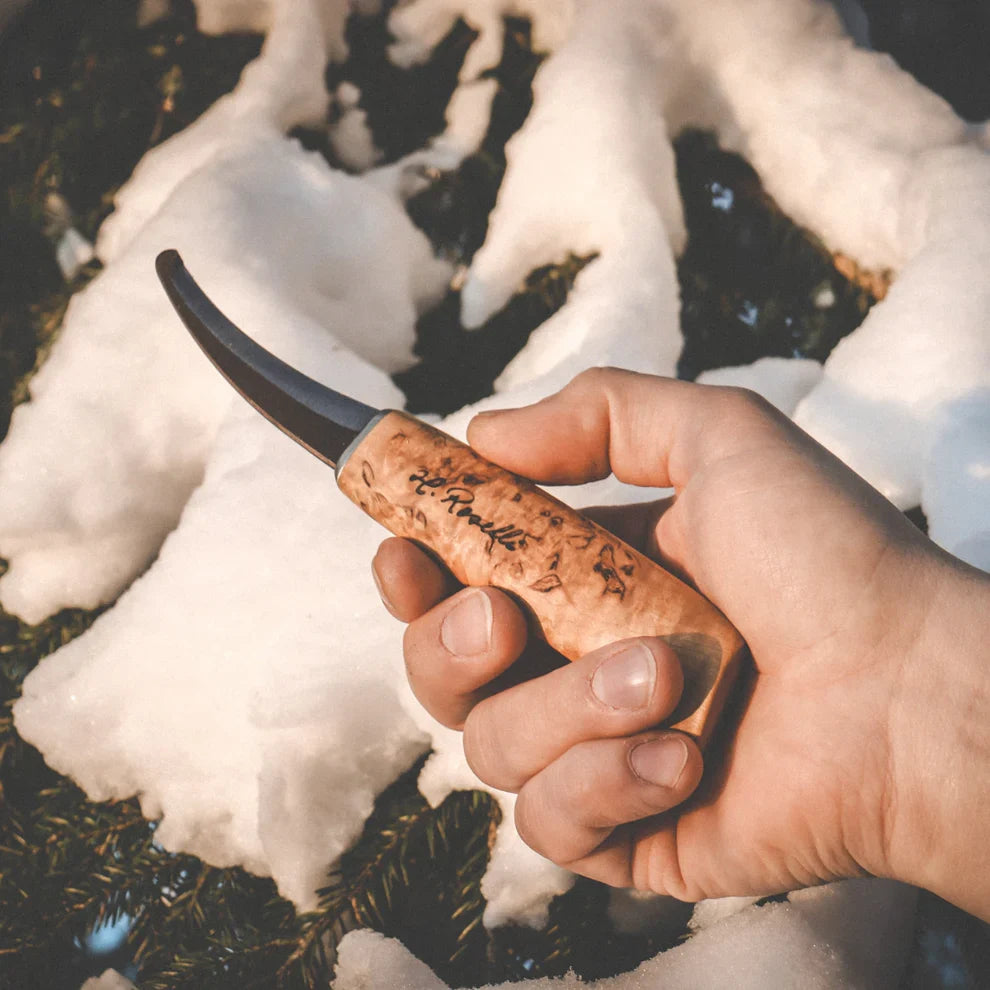Hand holding curved hunting knife with wooden handle in snowy forest