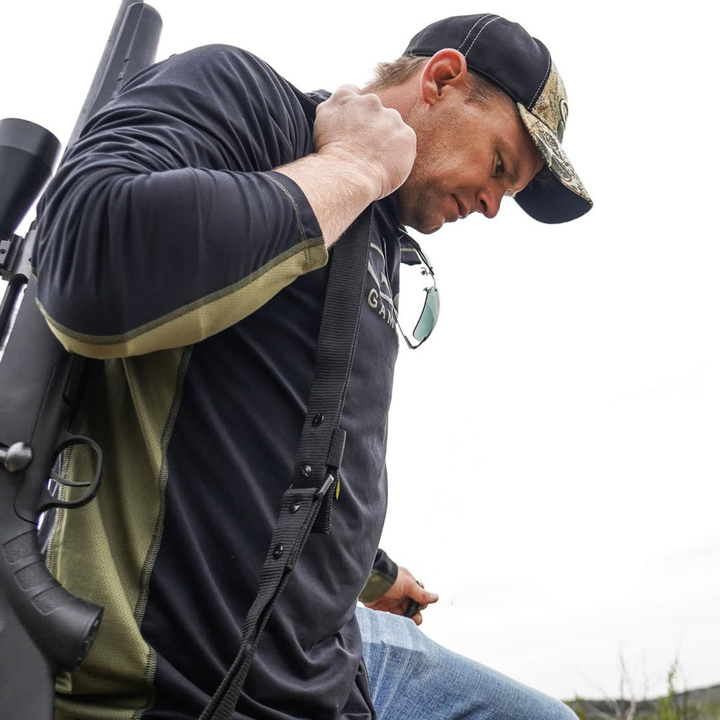 Hunter in camo cap and long sleeve shirt carrying rifle, outdoor hunting gear