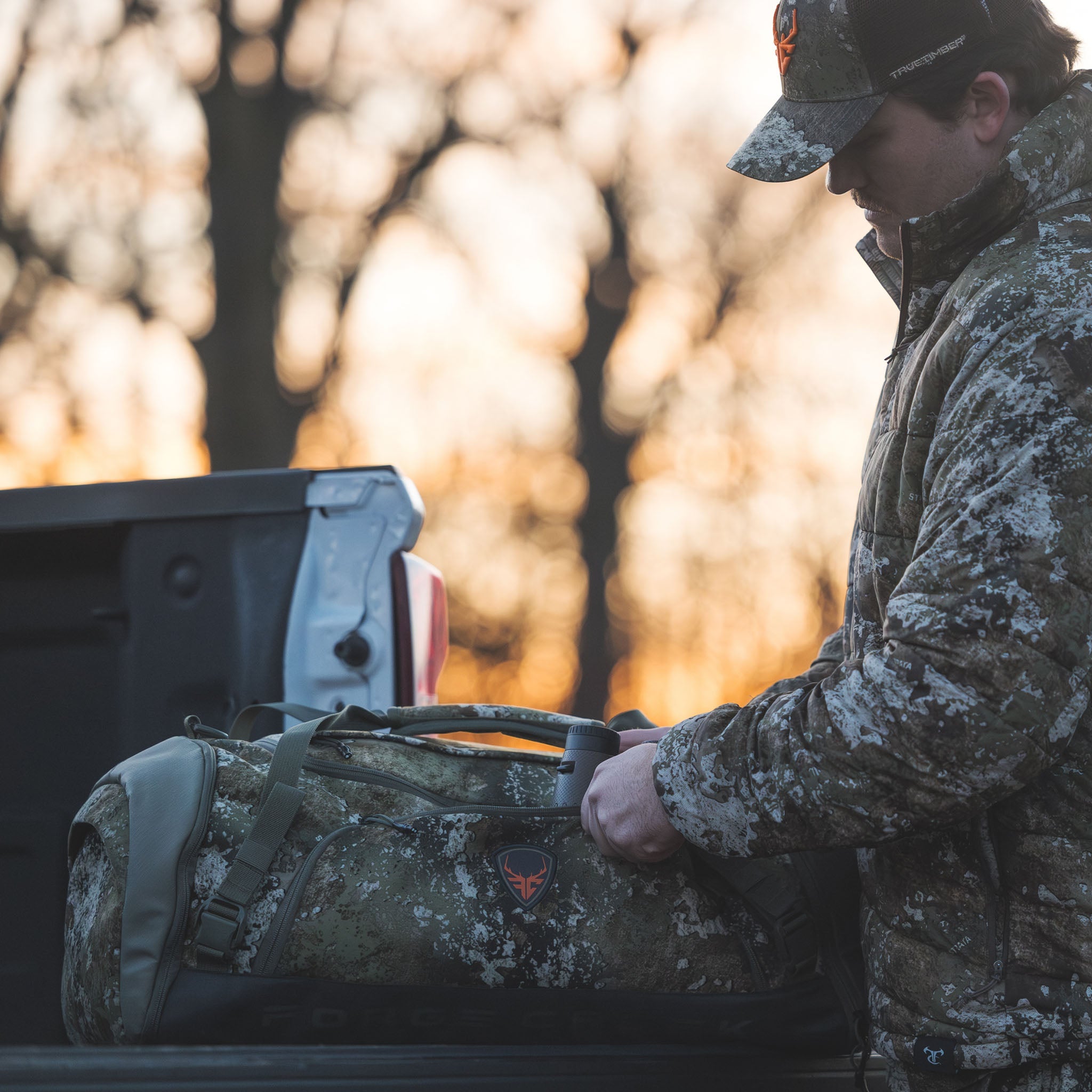 Hunter in TrueTimber camo gear with matching duffel bag, ready for outdoor hunting trip