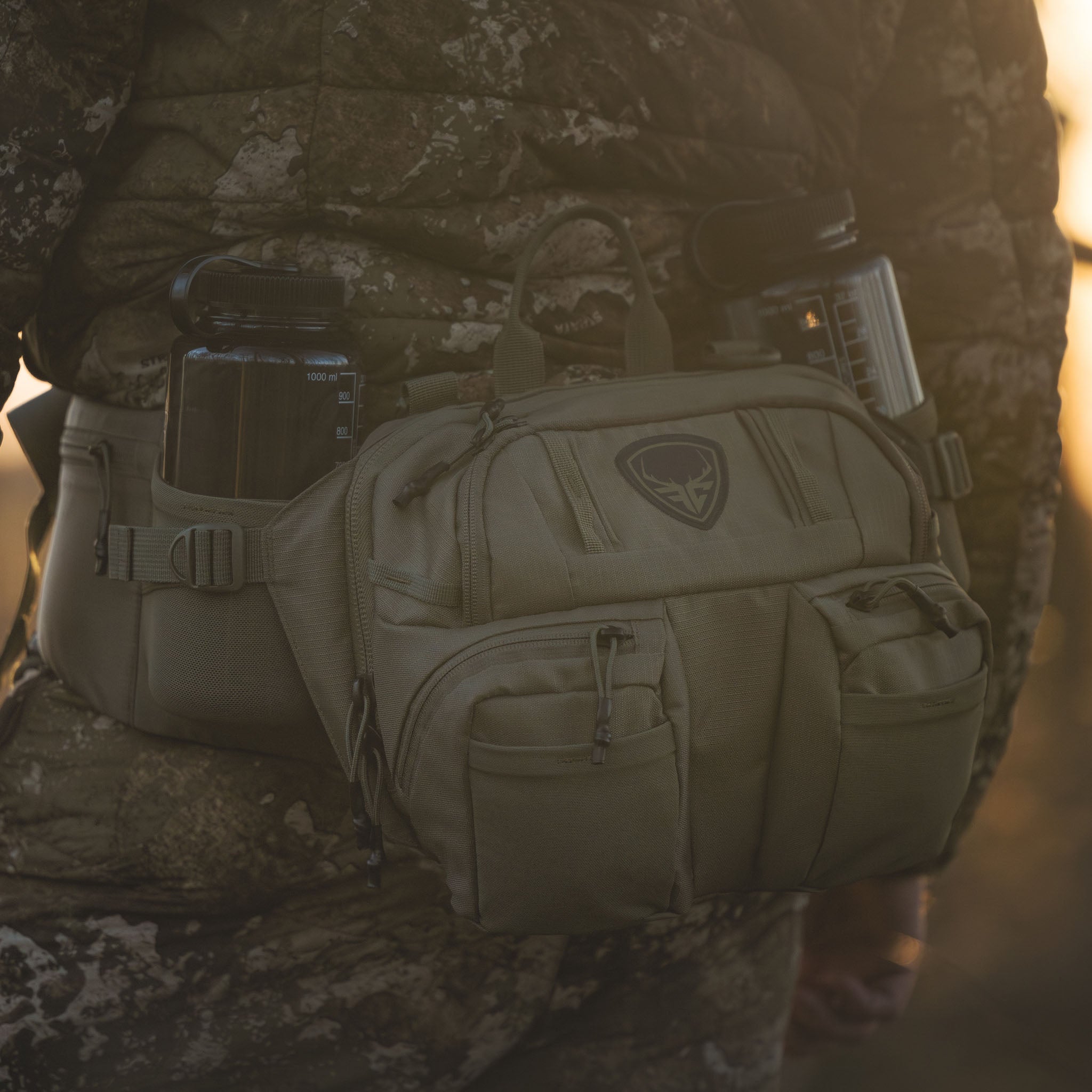 Tactical waist pack with water bottle holders, worn over camo hunting gear for outdoor adventures