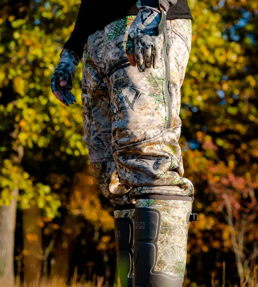 Hunter in Vycah Kinsley Pants and rubber boots climbing a ladder stand in fall timber