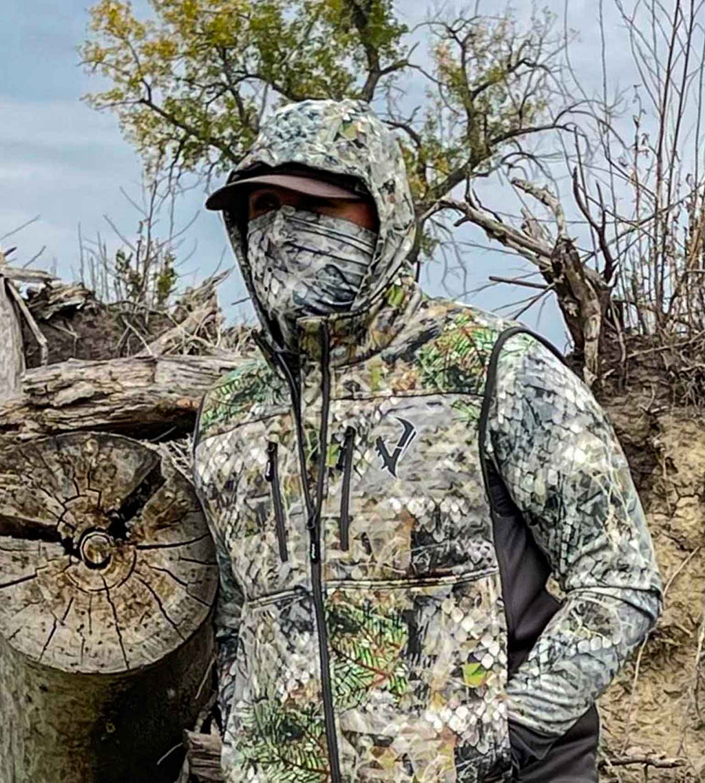 Hunter wearing a Vycah Kinsley Vest over a camo hoodie with a face mask, standing in brush