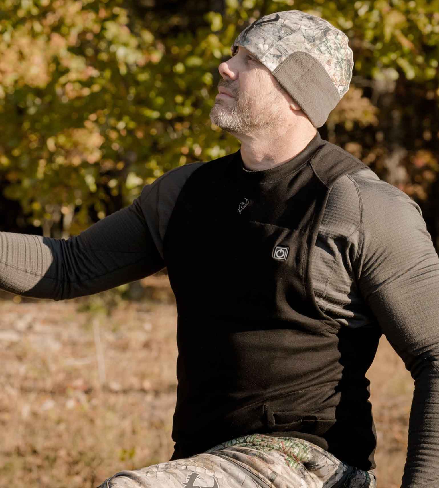 Hunter wearing a Vycah Oculus Heated Vest over a base layer with a camo beanie in fall timber